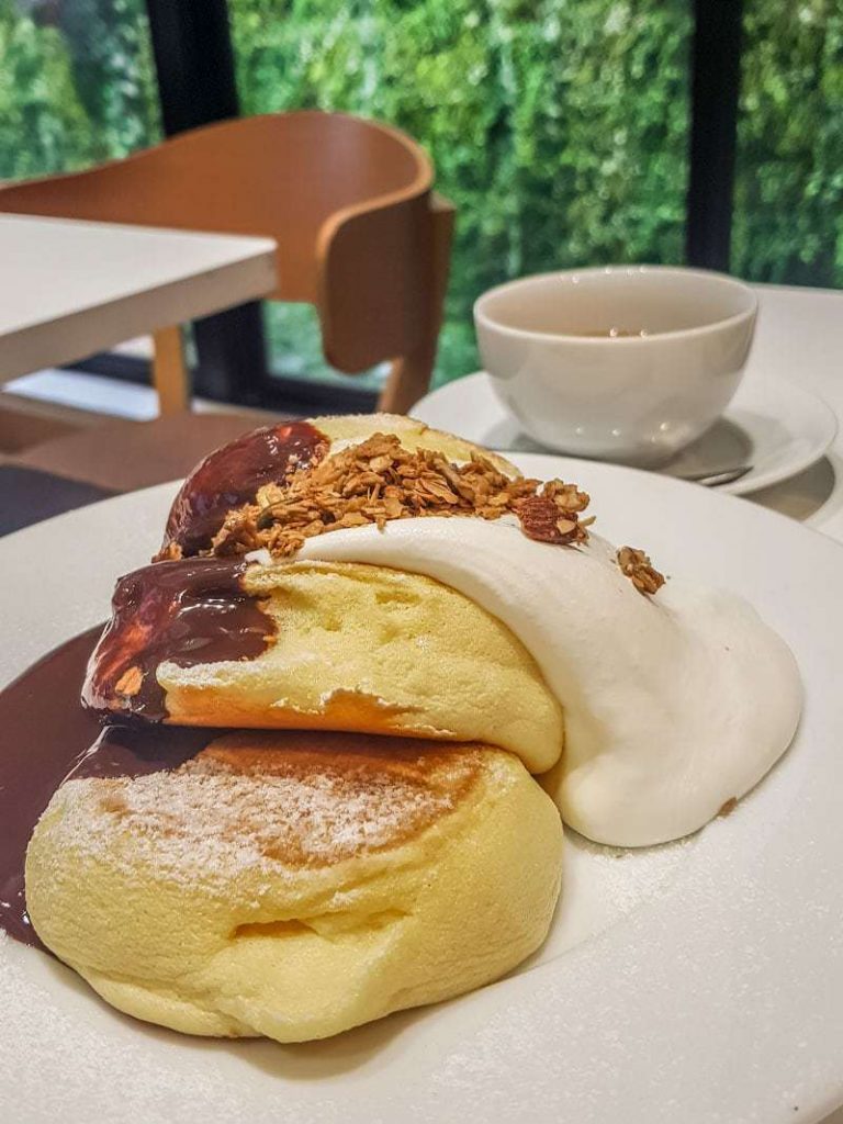 Souffle pancakes with chocolate sauce, granola and cream with backdrop of vines outside the window at A Happy Pancake in Shibuya, Tokyo