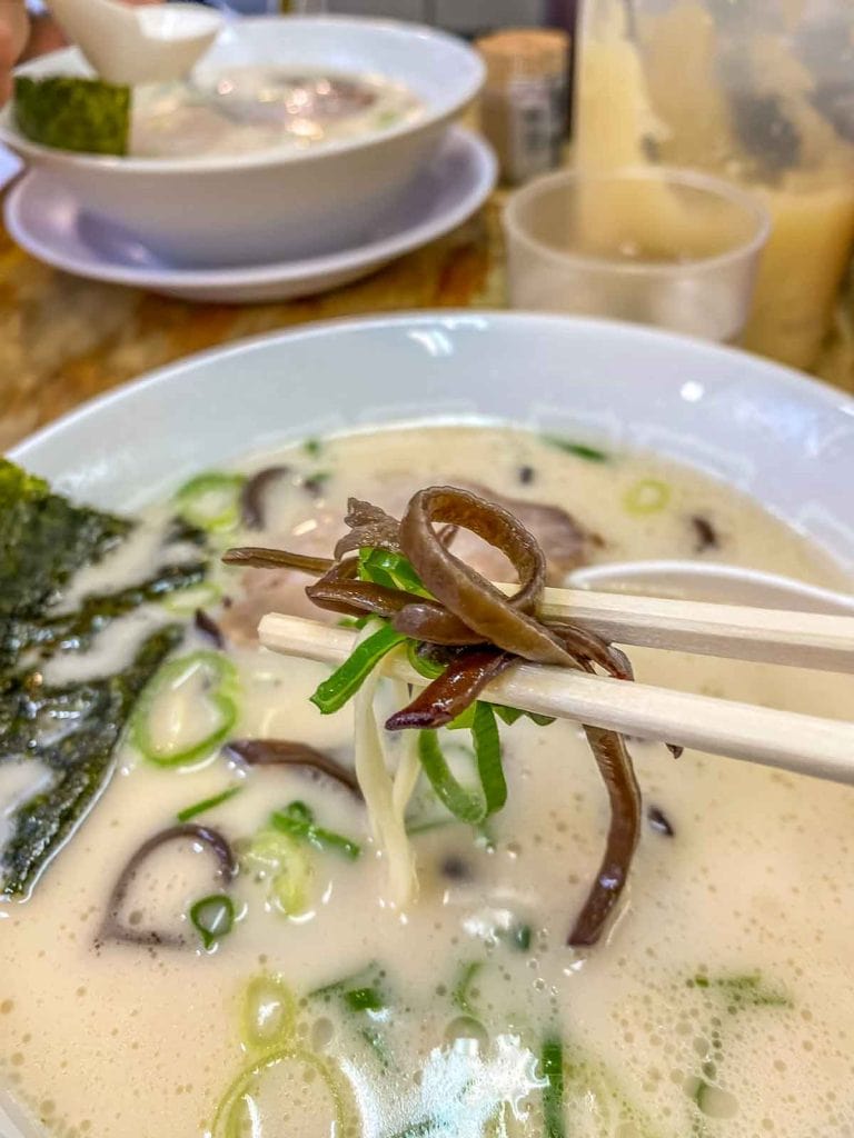 Pork broth ramen with mushrooms held in chopsticks